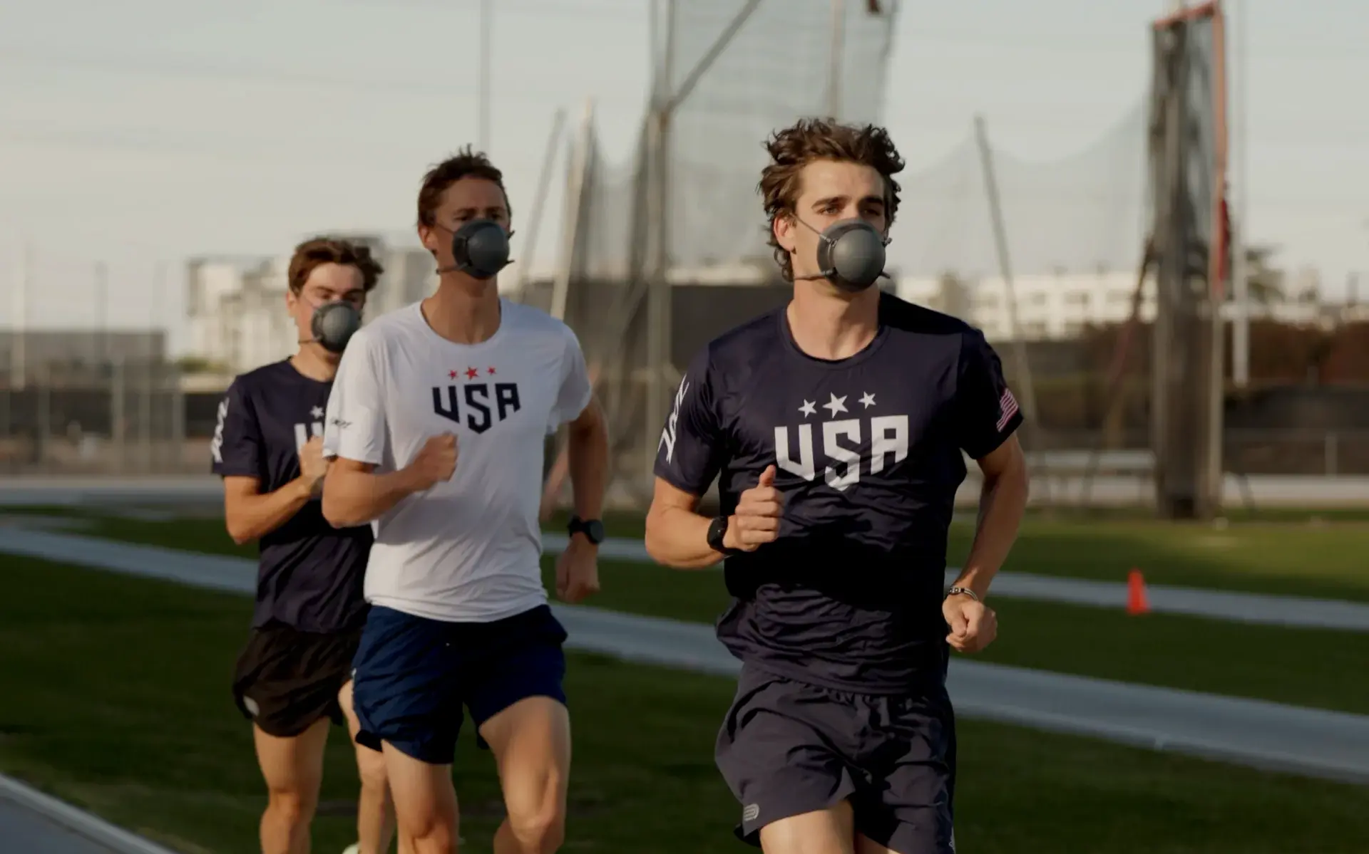Three USAT athletes running on an outdoor track during the day, wearing PACER